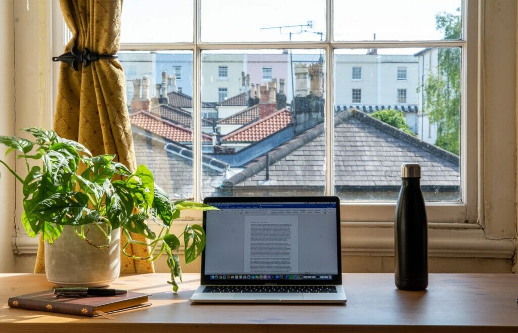 Photo of a laptop sitting on a desk with a view of a city outside the window